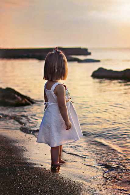 夕焼けの浜辺に佇む女の子の後姿を撮影したノスタルジックな写真素材