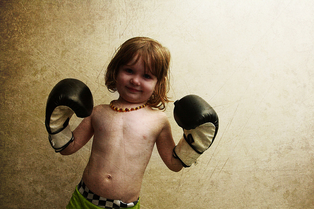 ボクシンググローブをはめて微笑む男の子の写真素材。ブラウン系の色合いとグランジ感がクール。