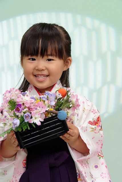 花を持って笑いかける女の子の七五三の写真。背景のブルーとピンクの着物が爽やか。