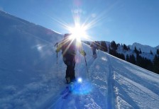 スキーを履いて雪山を登るところを撮影した写真素材。澄み切った青空に輝く太陽の逆光が綺麗。