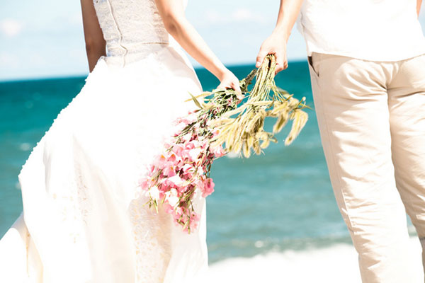 海辺の白い砂浜の花束を持ったカップルの写真。幸せそうな雰囲気が結婚にぴったり。