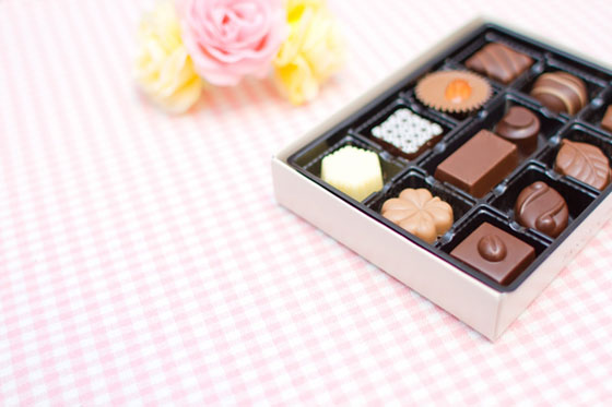 チョコレートの詰まった箱とピンクのバラの花飾りの写真素材。バレンタインデーのデザインに。